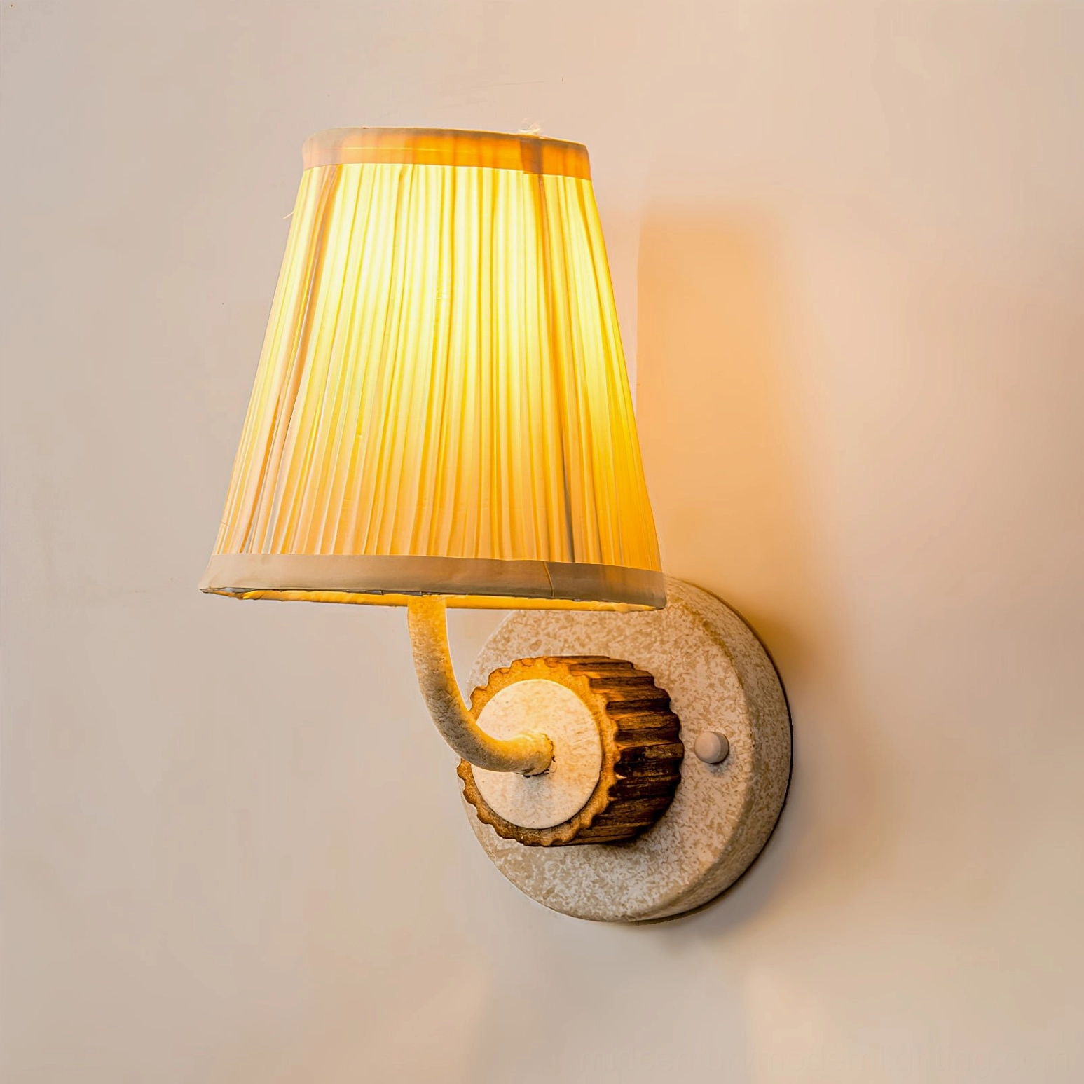 Abbey wall sconce lit from left angle highlighting pleated shade and warm ambiance