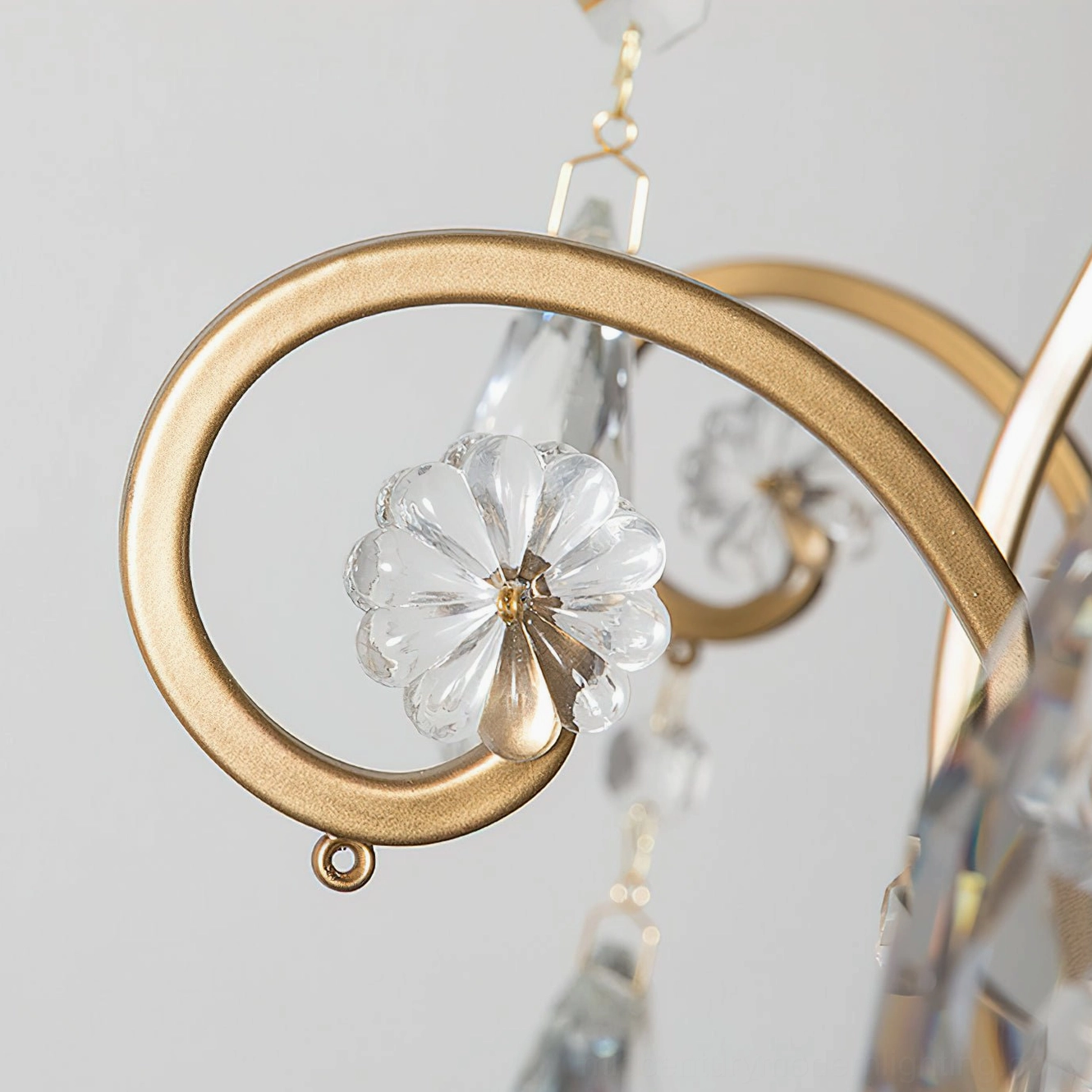 Detailed macro photograph of Aeliana Crystal Chandelier gold scroll metal frame with flower-shaped crystal ornament and glossy metallic texture