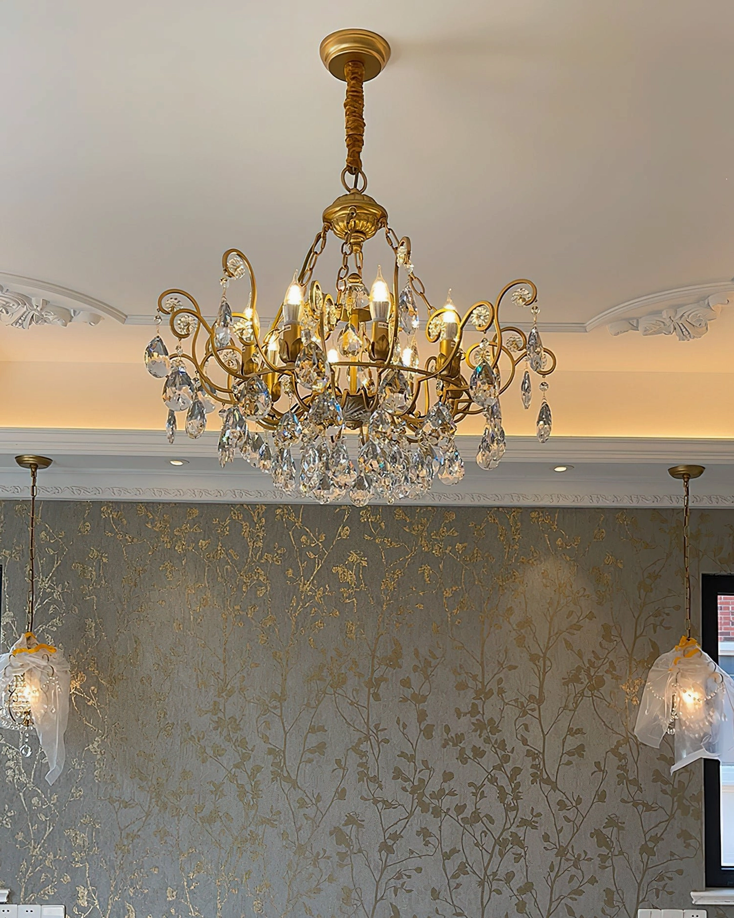 Matching Aeliana Crystal Chandelier and pendant lights set in bedroom with patterned wallpaper featuring gold vintage American style lighting ensemble