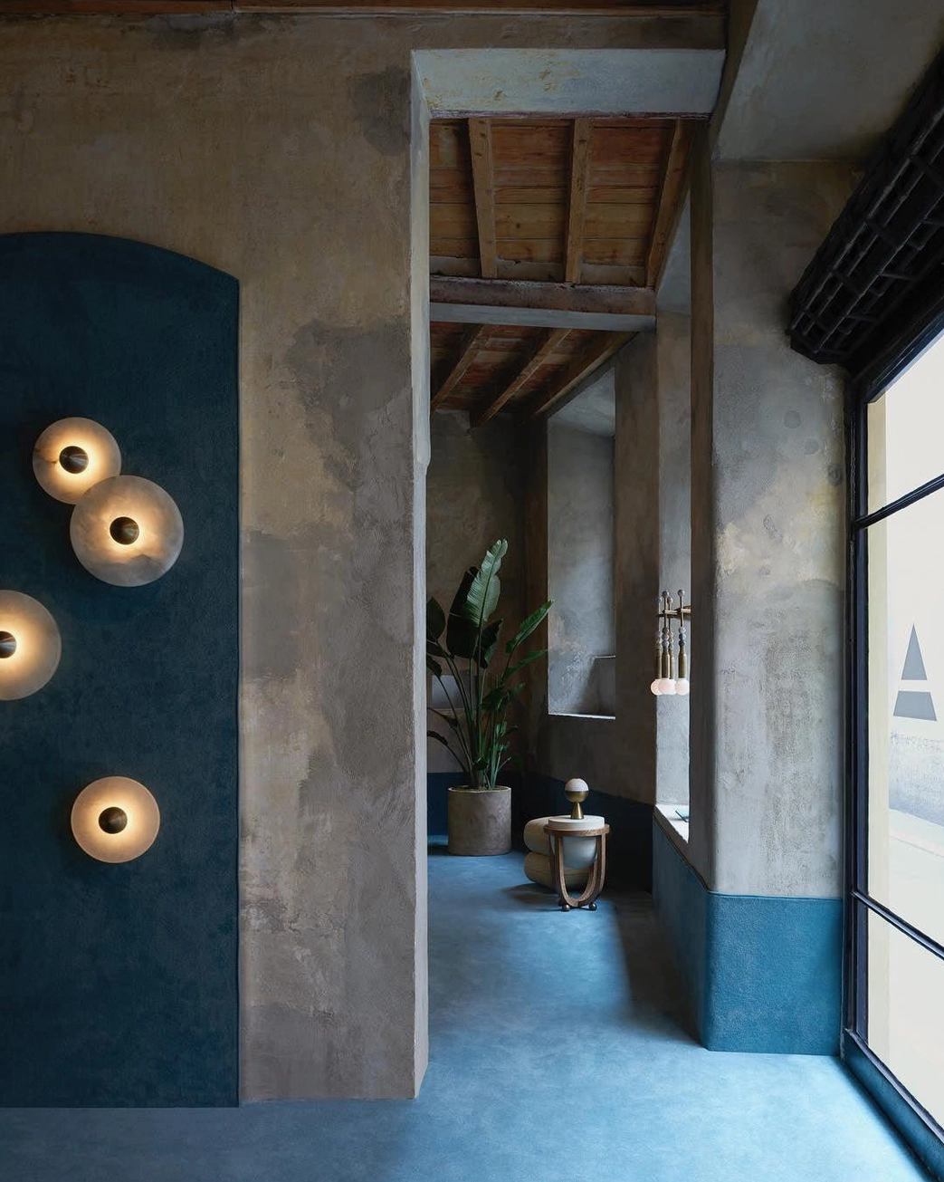 Industrial minimalist apartment hallway with round alabaster wall lights, concrete walls, blue floor, warm ambient glow