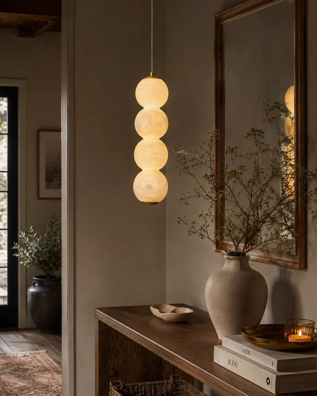 Sculptural pendant light reflecting in mirror above entryway console warm brass accent