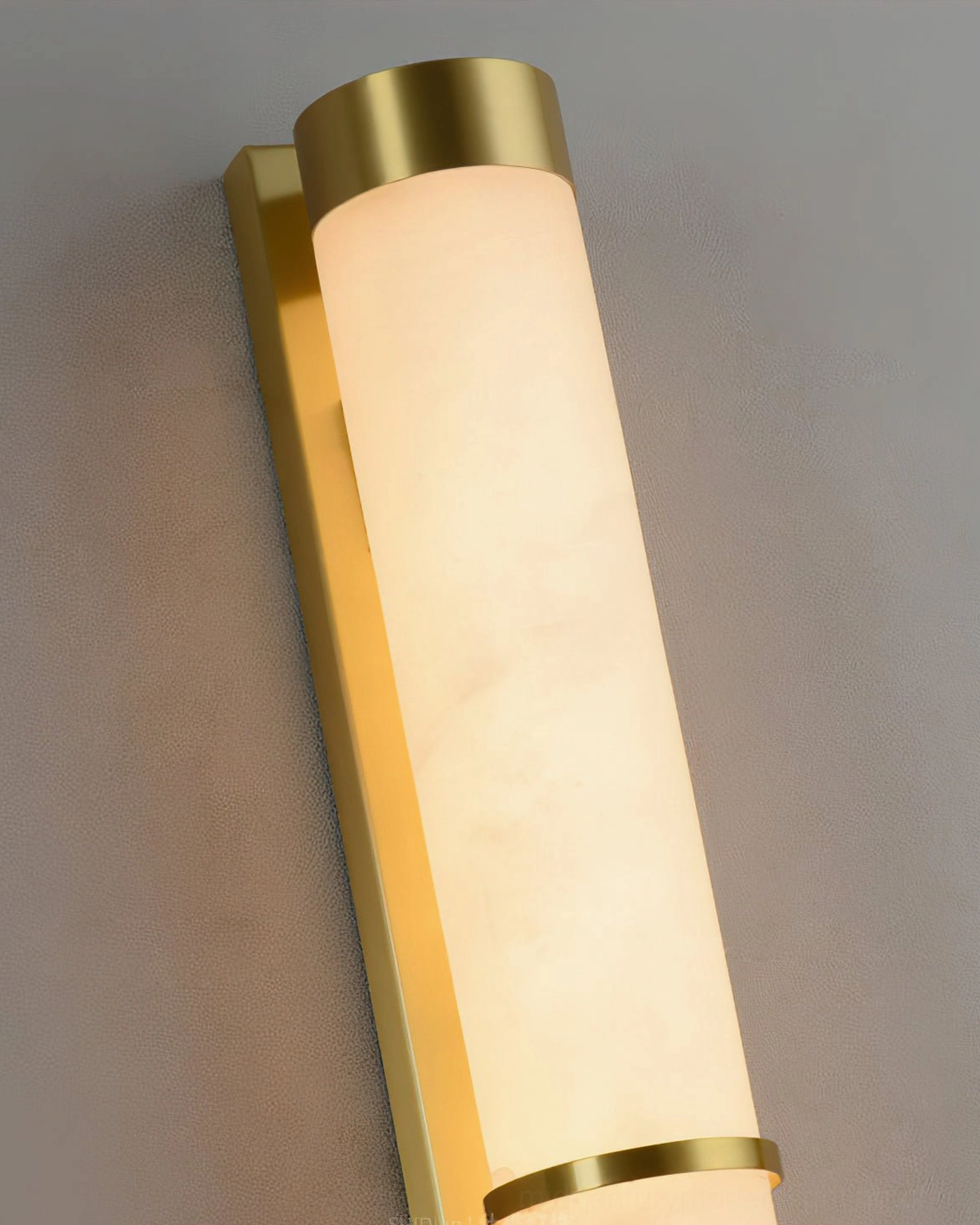 Close-up detail of alabaster wall sconce with brass gold end caps and middle trim bands, warm illuminated light