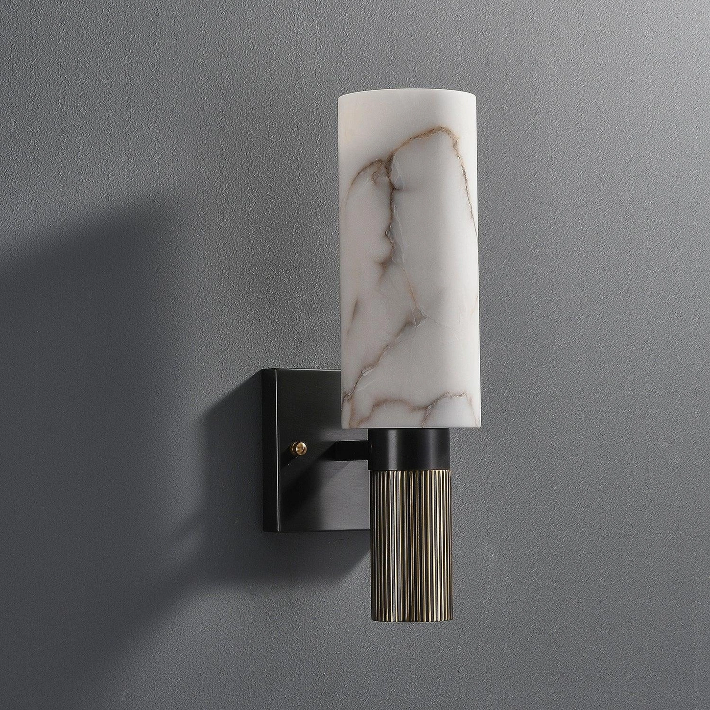 Unlit alabaster wall lamp mounted on grey wall, matte black bracket and cylindrical marble shade visible
