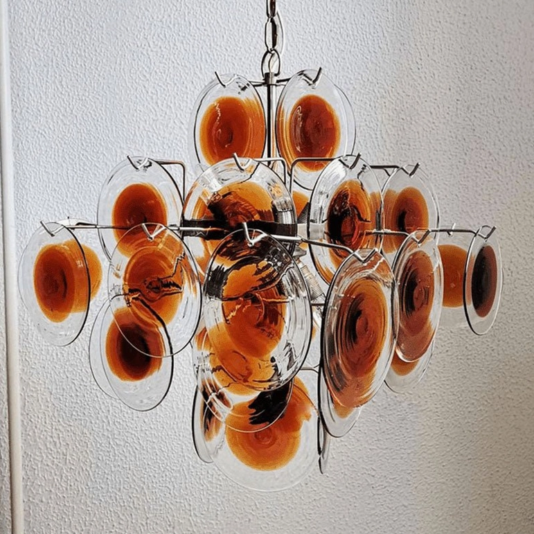 Hand-blown amber glass discs close-up detail showing chrome metal framework and artisanal craftsmanship