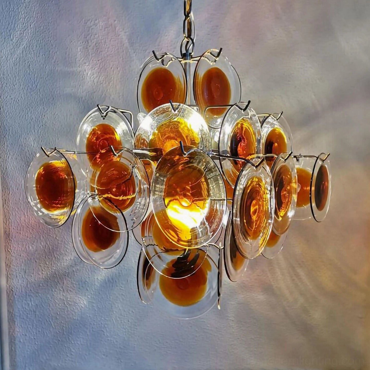 Illuminated amber glass disc chandelier against accent wall showcasing light diffusion and glow