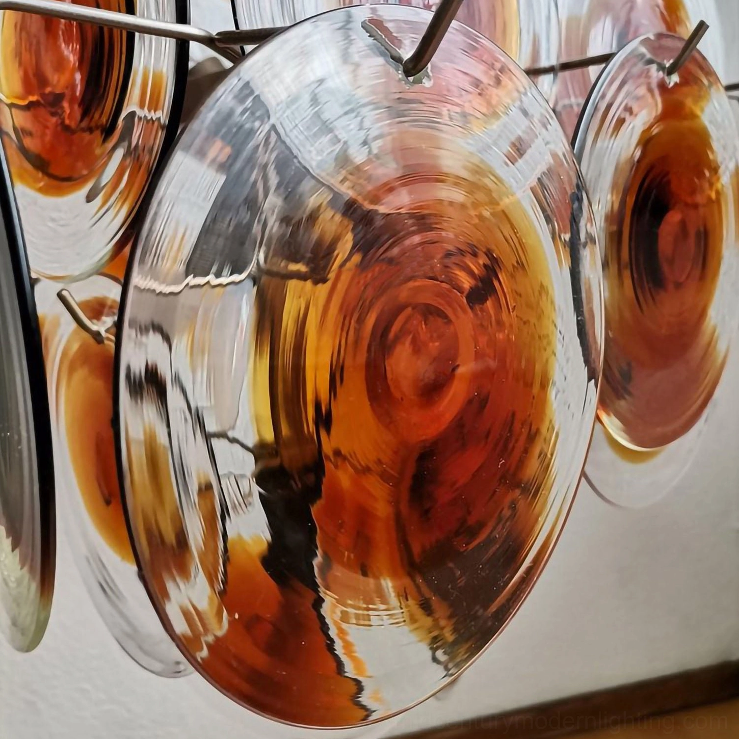 Side-angle view of thick reflective amber glass discs with metal hanging clips and suspension system