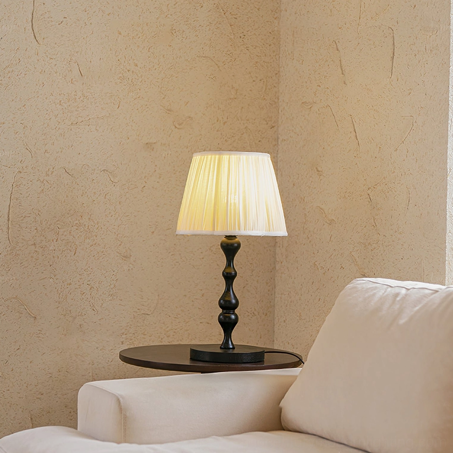 Modern pleated fabric lamp with dark wooden base illuminated beside contemporary beige sofa and compact side table