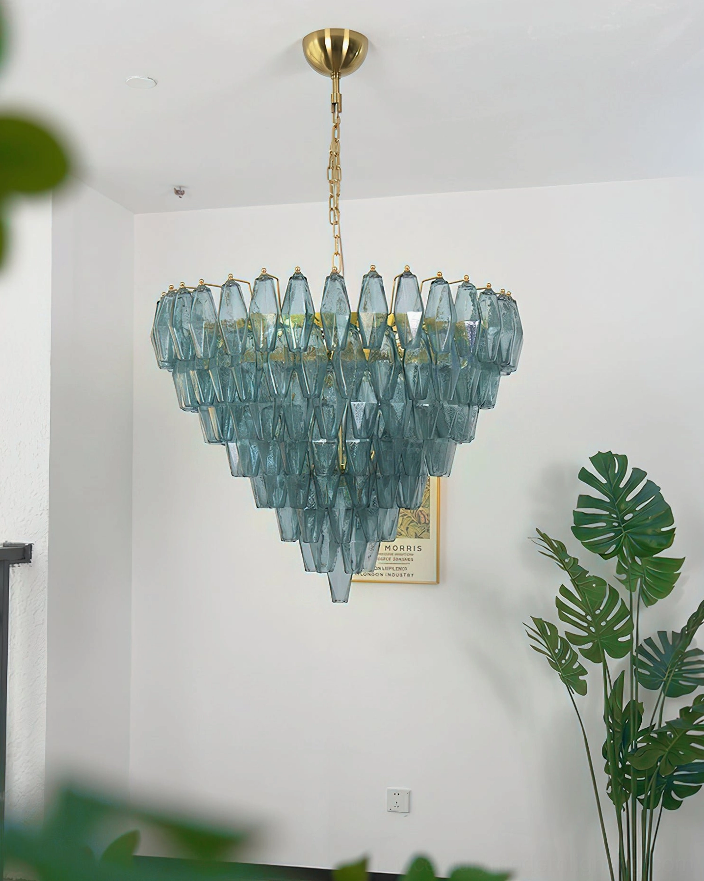 Blue and gold Ametista geometric chandelier installed in minimalist home interior with monstera plant and contemporary decor