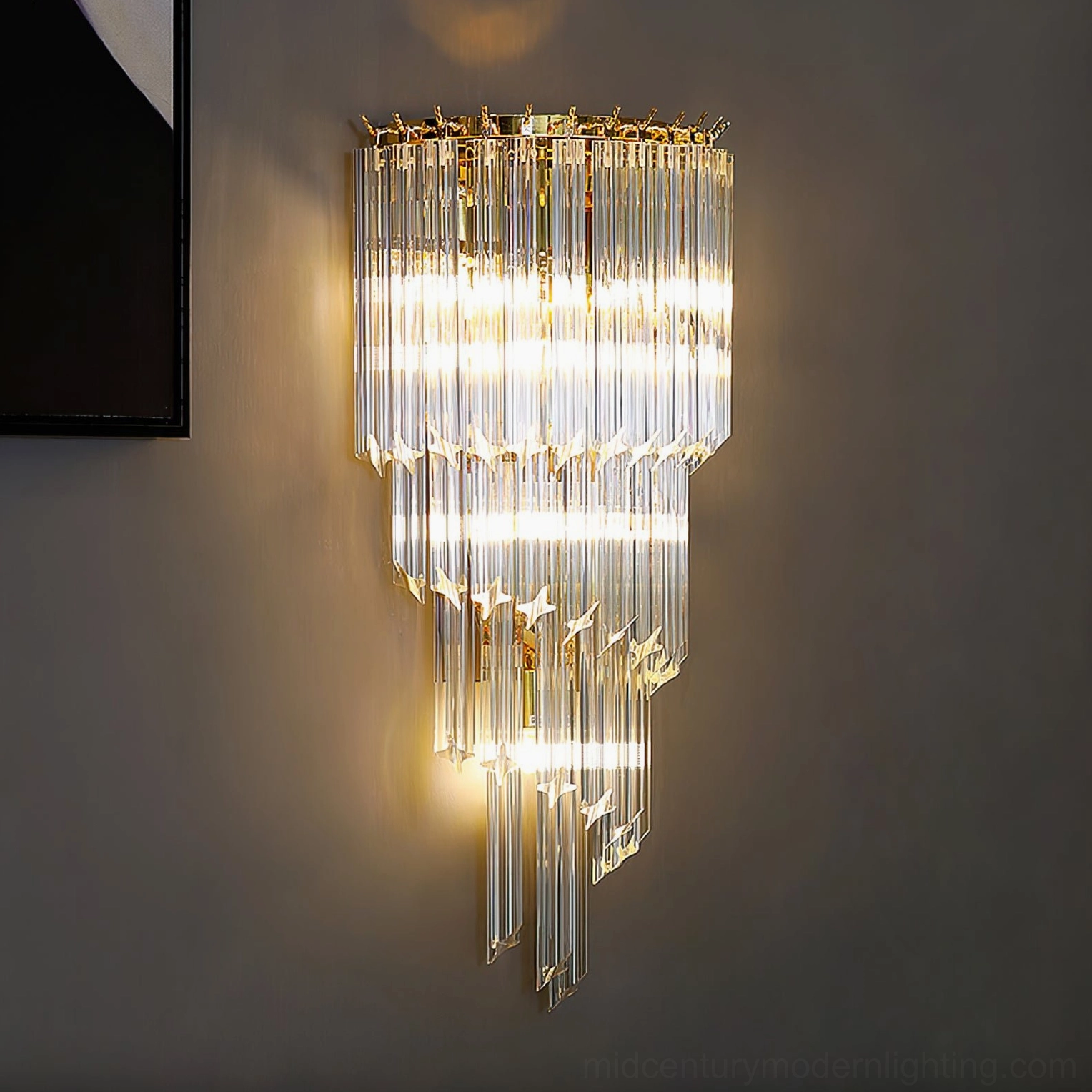 Fully illuminated tiered crystal wall sconce on dark gray wall with black wall art, atmospheric lighting