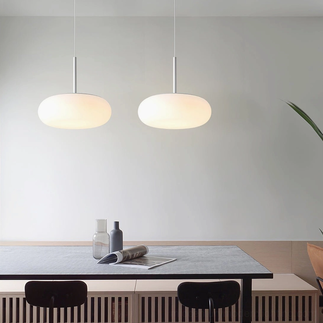 Two matching Amor white pendant lamps suspended above long dining table, coordinated minimalist hanging light installation