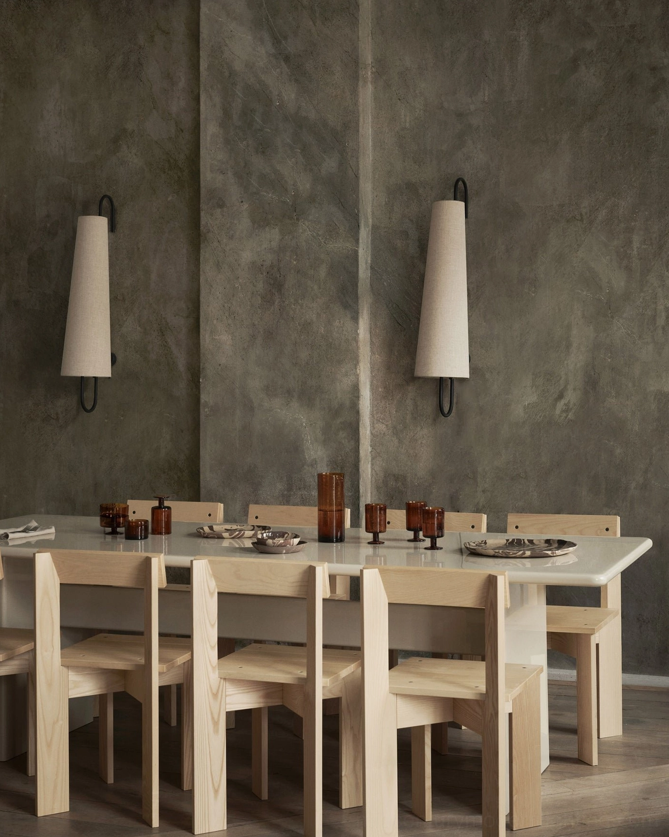 Two Ancora wall lamps flanking modern dining room with natural wood table and decor on cement wall backdrop