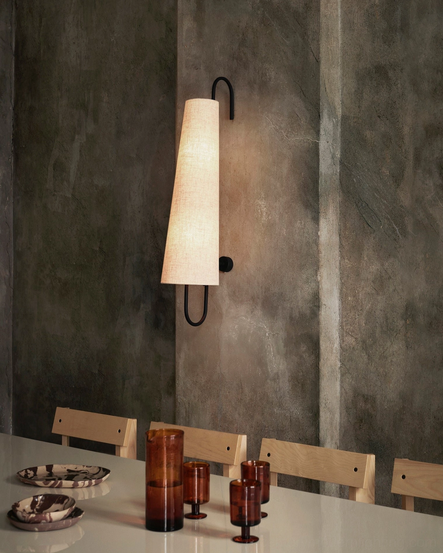 Ancora wall lamp with lit warm glow above dining table with amber glass tableware and place settings