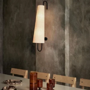 Single Ancora wall lamp mounted in contemporary dining room with cement wall, warm glowing linen shade creating ambient lighting