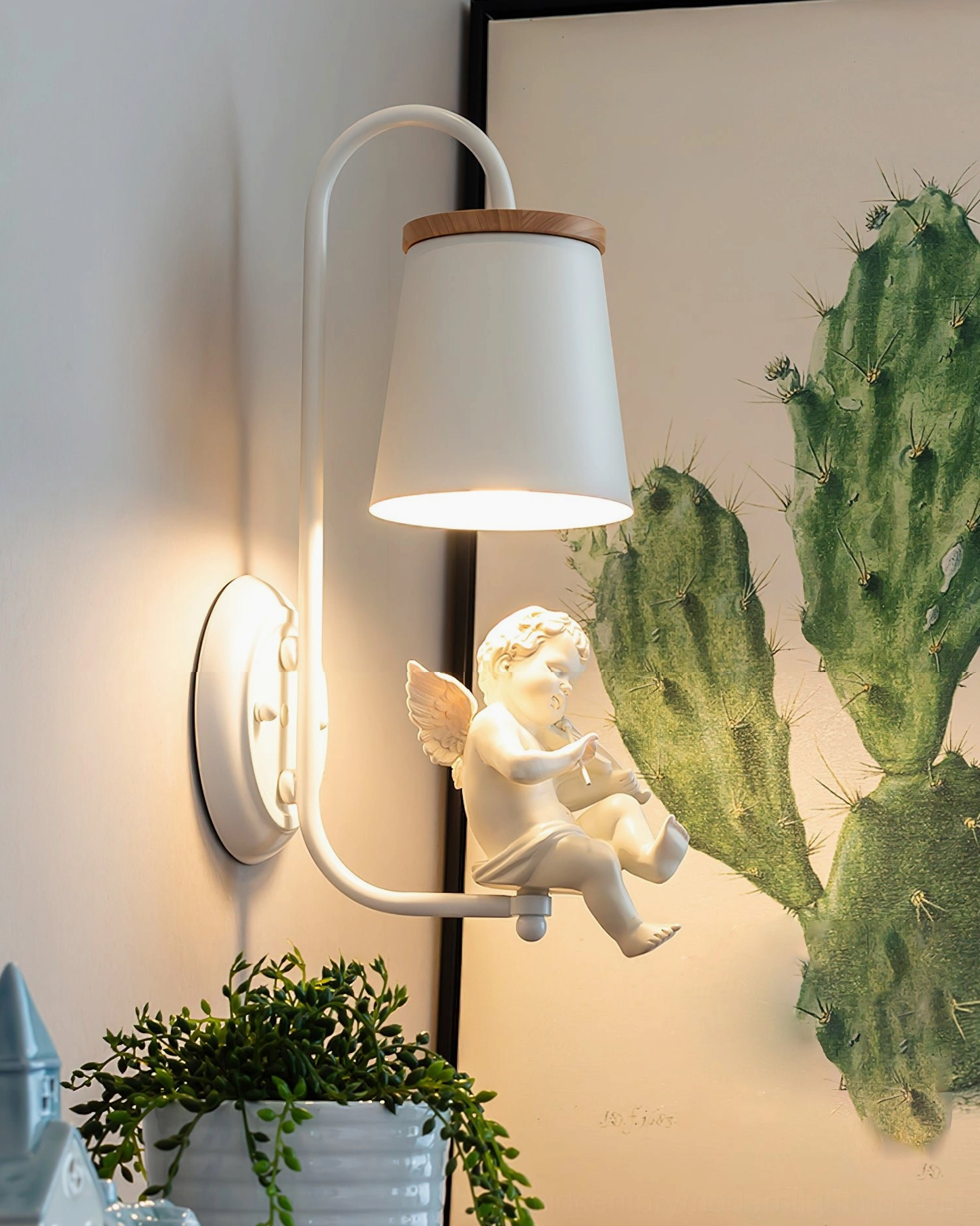 Sitting cherub wall light fixture with flute on beige wall with cactus botanical home decor elements