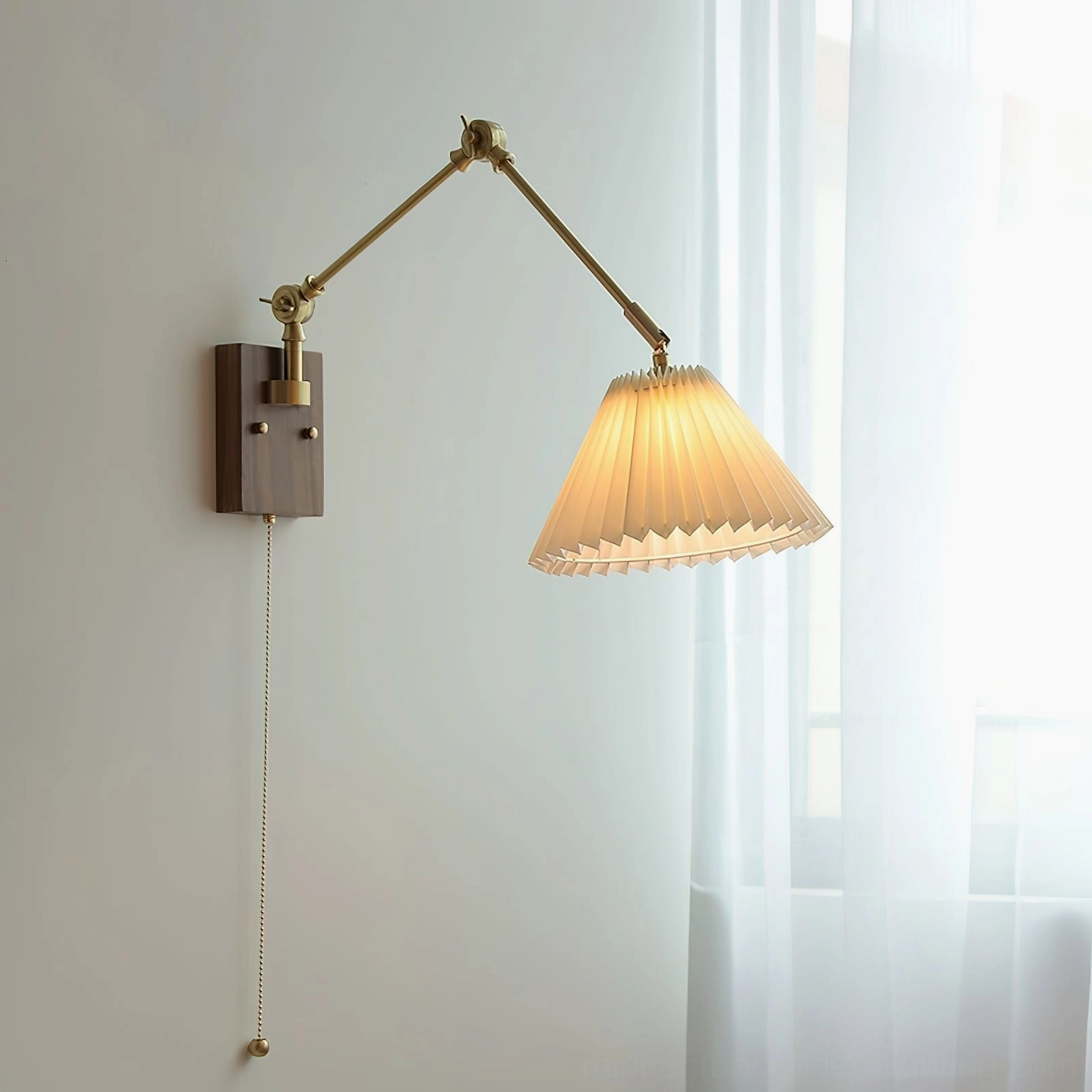 Angeline swing arm wall lamp lit in room setting with sheer curtains, side three-quarter view showing pleated shade illumination and brass articulated arm