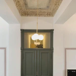 Polished brass and frosted glass globe pendant light installed in vintage entryway with ornate ceiling and dark green cabinet