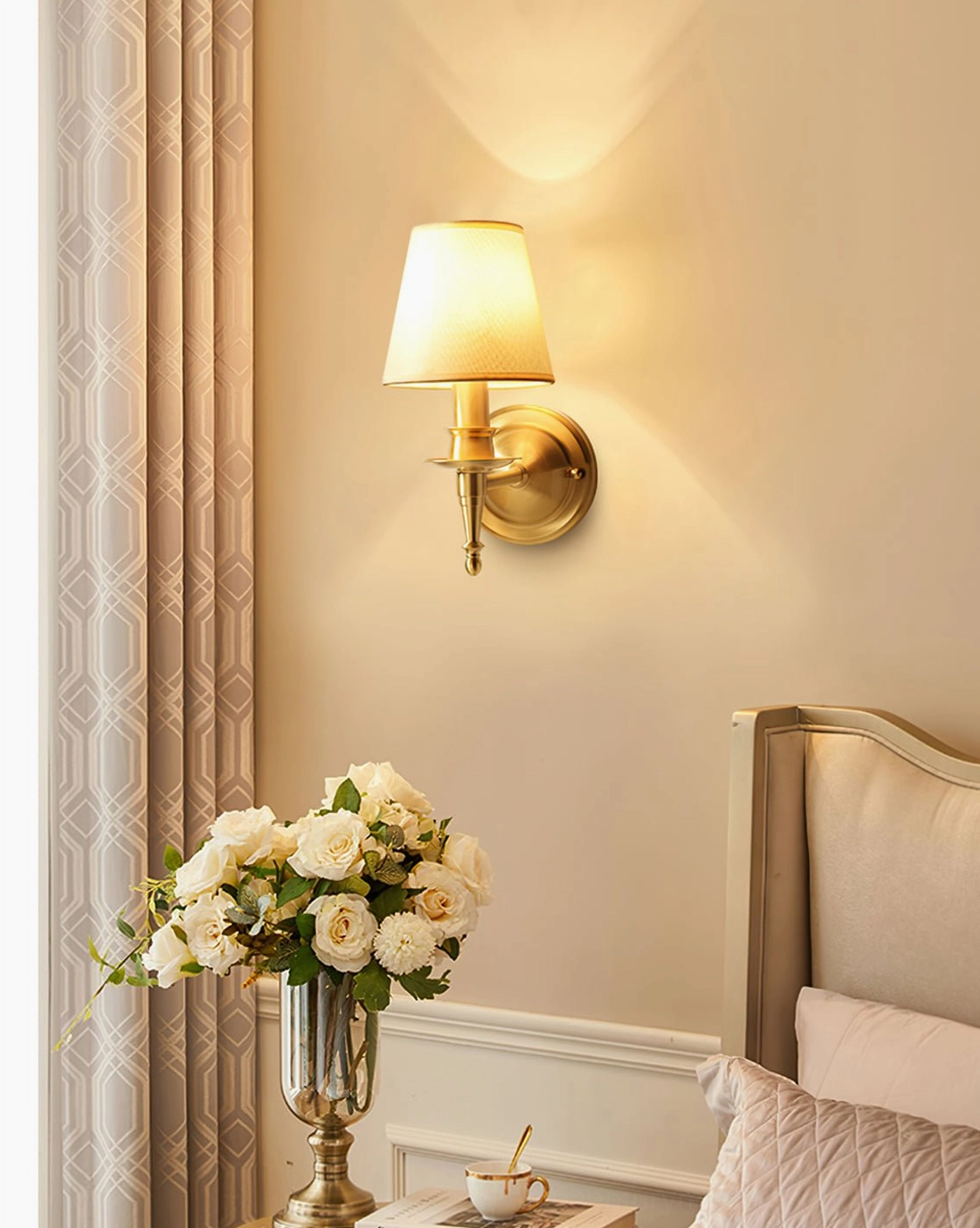 Antique brass wall sconce in bedroom bedside arrangement with flower arrangement and warm glow