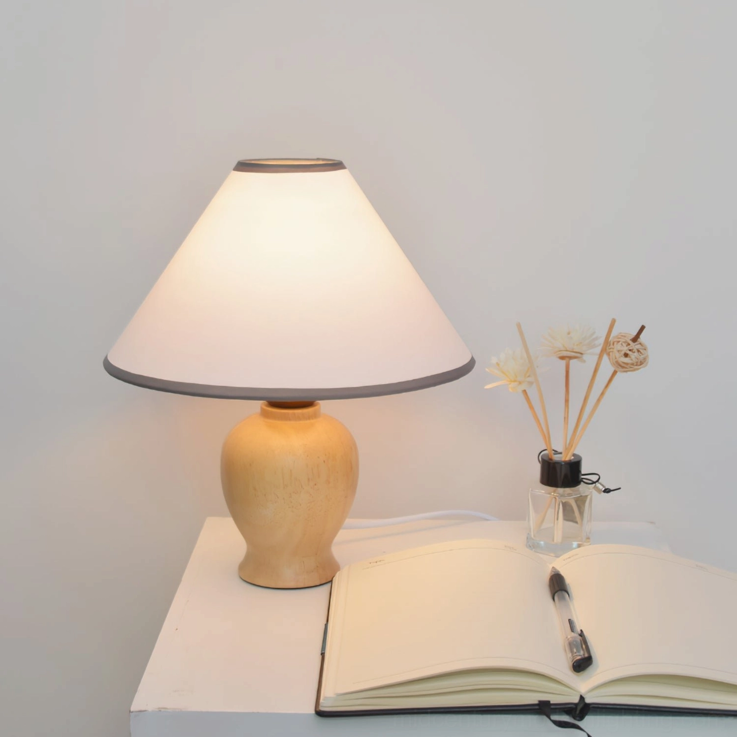 Minimalist home decor setup with Arbol table lamp on white surface surrounded by open notebook and reed diffuser, cozy aesthetic