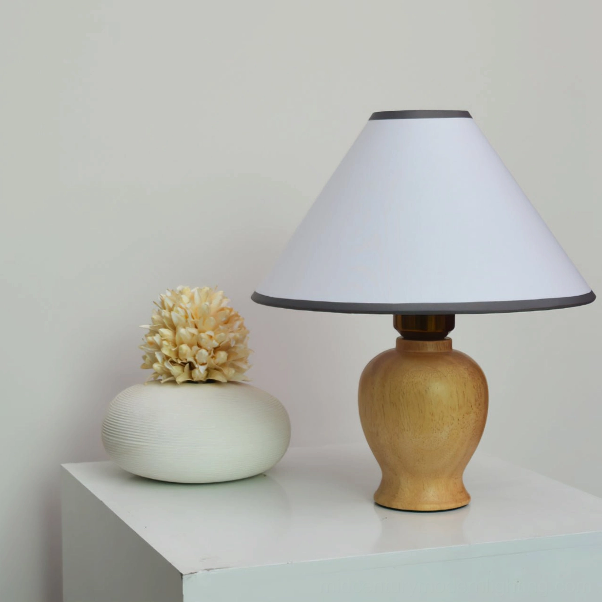 Side profile view of Arbol lamp base showcasing smooth wood grain urn-shaped silhouette with dried flower arrangement nearby