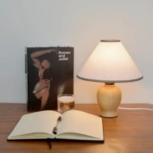 Arbol mid-century modern lamp positioned on wooden study desk with book and candle, three-quarter angle showing natural wood finish
