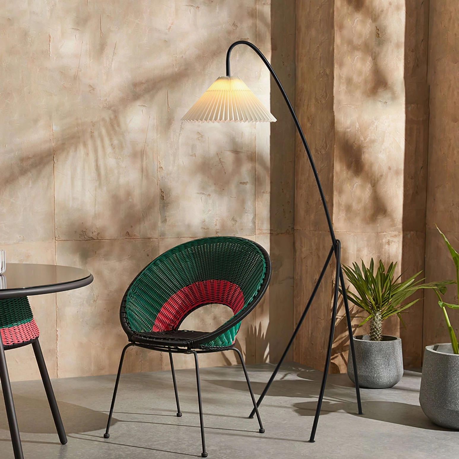 Arc tripod lamp with pleated shade in bohemian dining nook with woven chair, three-quarter view demonstrating warm modern home decor styling