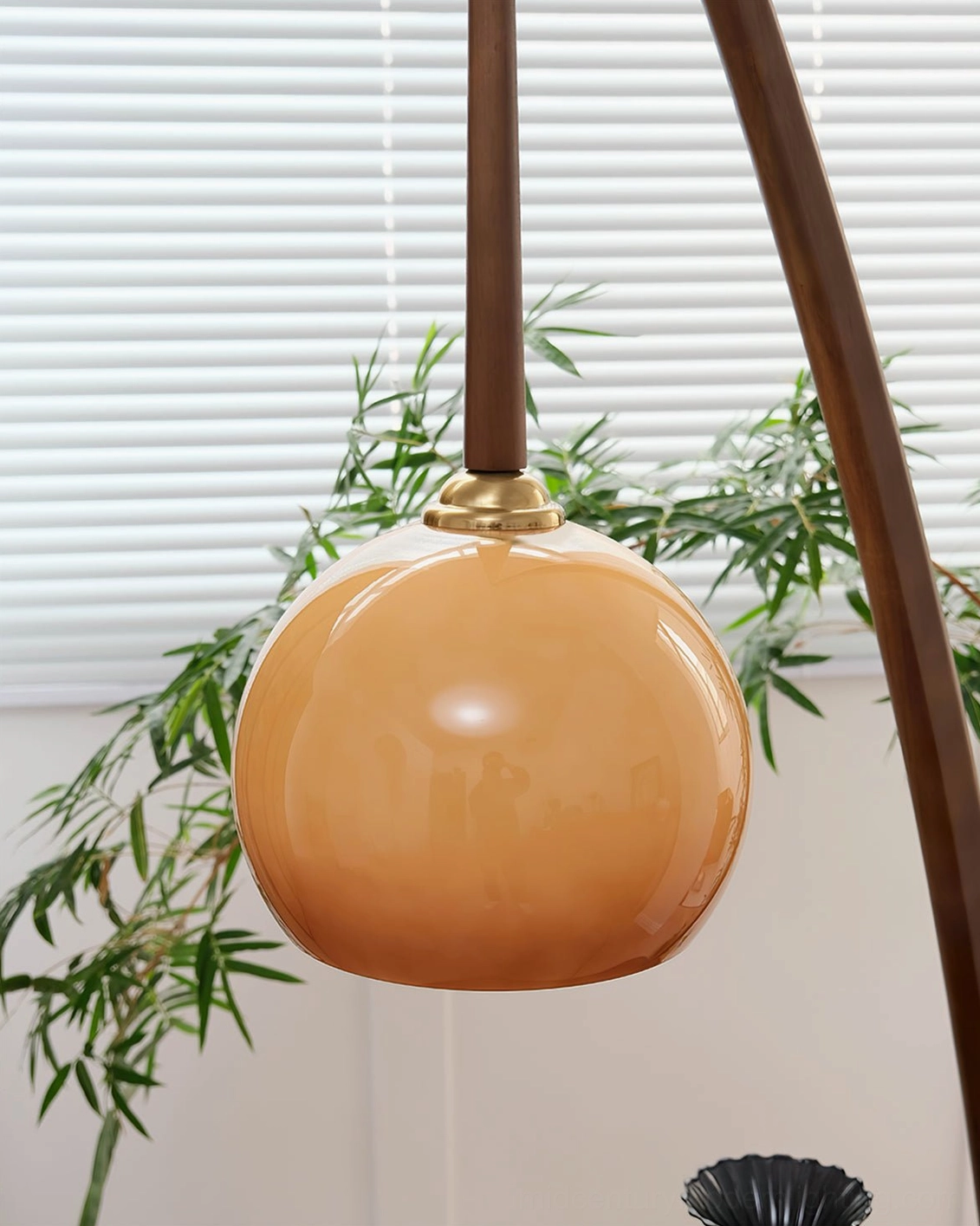 Close-up detail of arc floor lamp showing amber glass shade, brass joint, and walnut wood pole