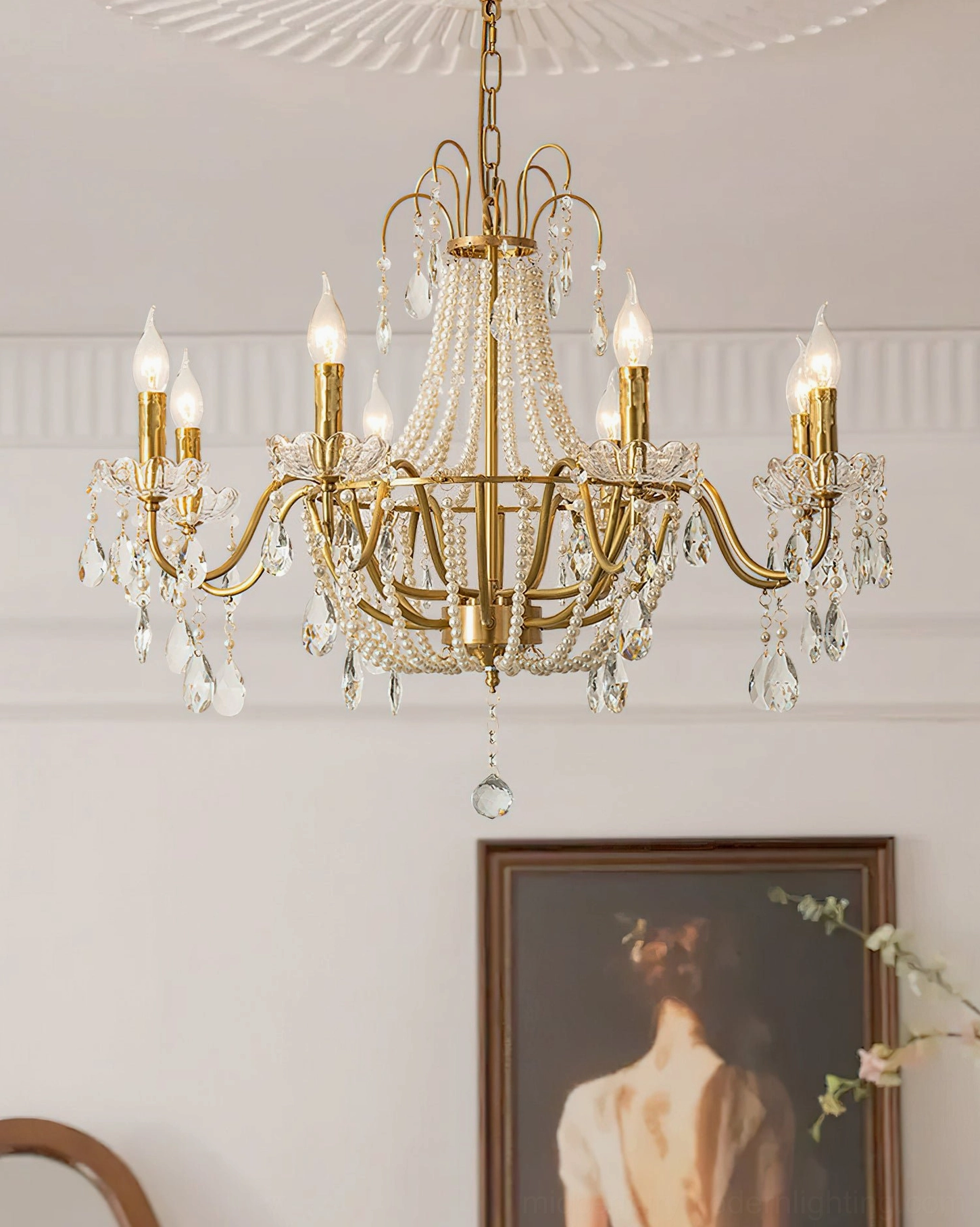 Arcadia brass chandelier with pearl beaded central design and lit candle bulbs on vintage wall art backdrop