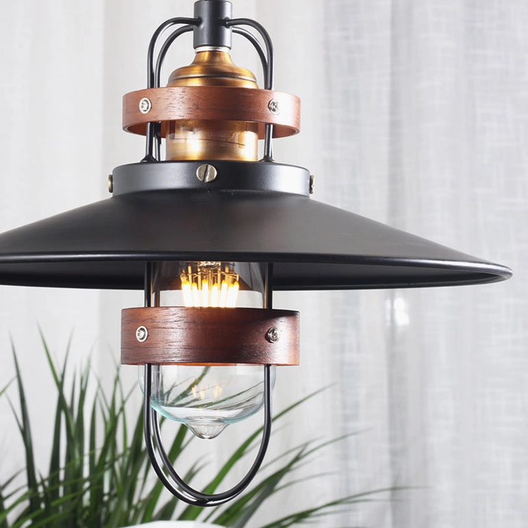 Arely pendant lamp close-up front view showing matte black shade, brass accents, walnut wood trim, and metal bulb protection cage