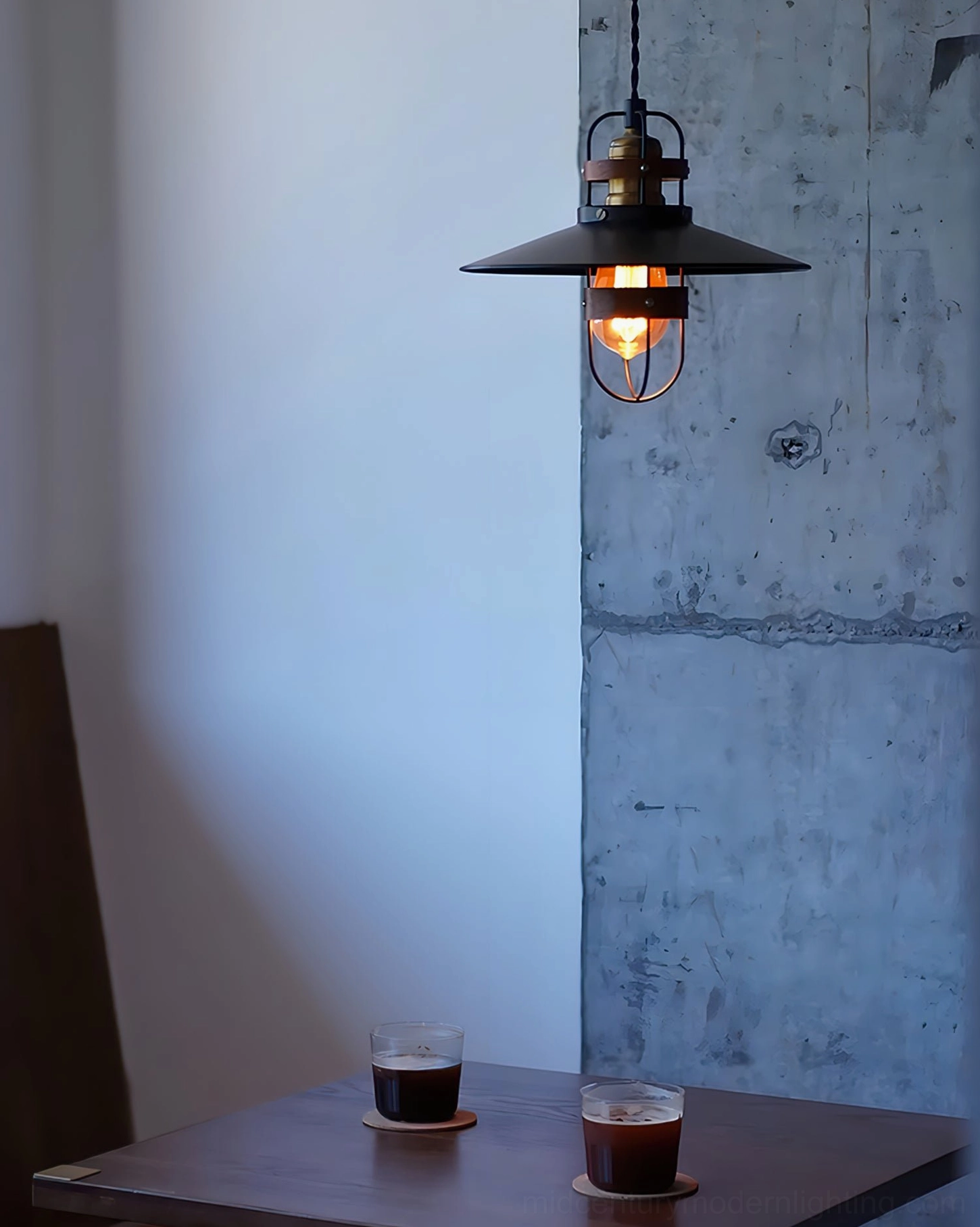 Arely industrial pendant lamp side view in minimalist dining nook with concrete wall, showing shadow patterns from cage