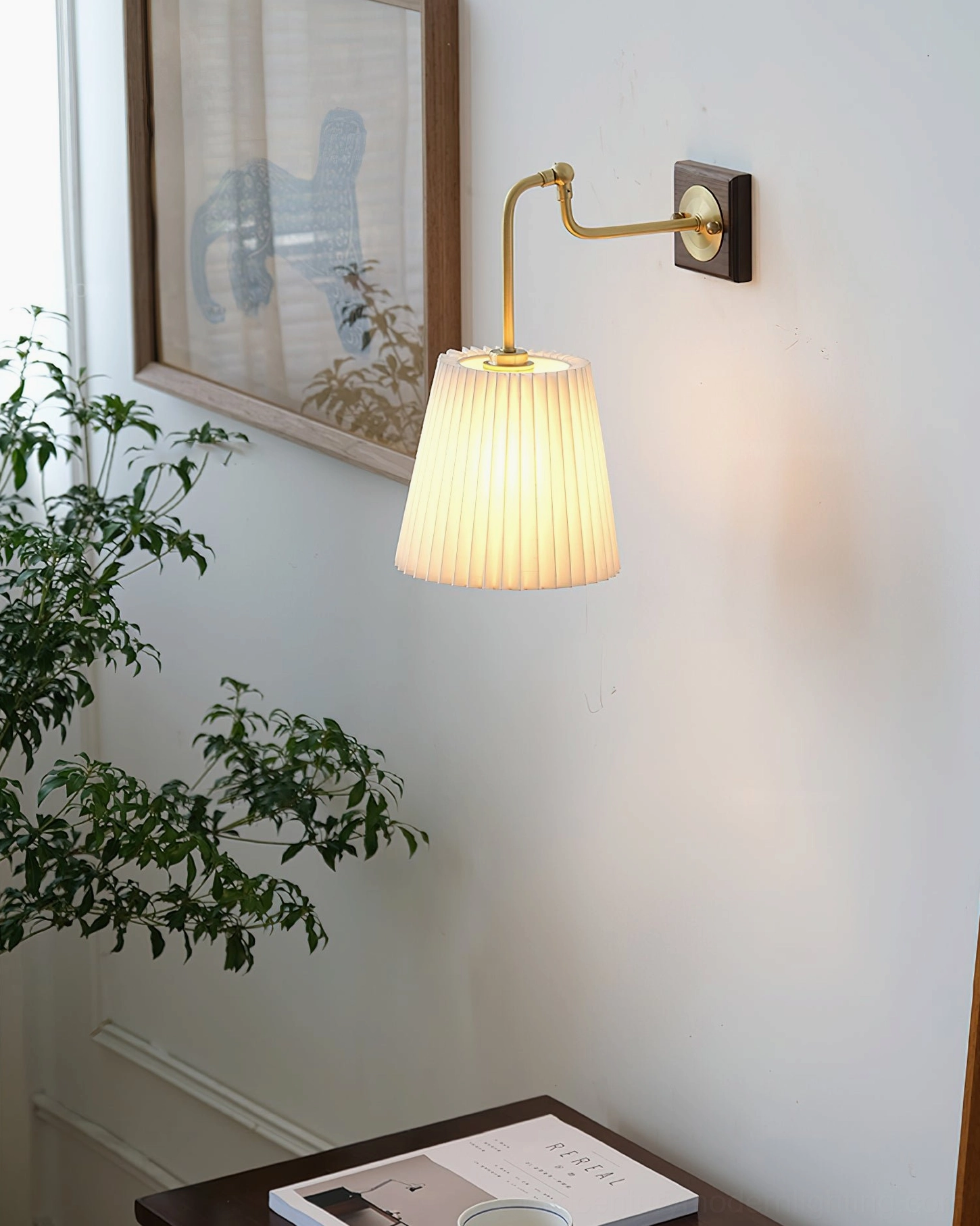 Argon wall lamp mounted three-quarter view showing pleated white shade and brass hardware in home interior with art and plant