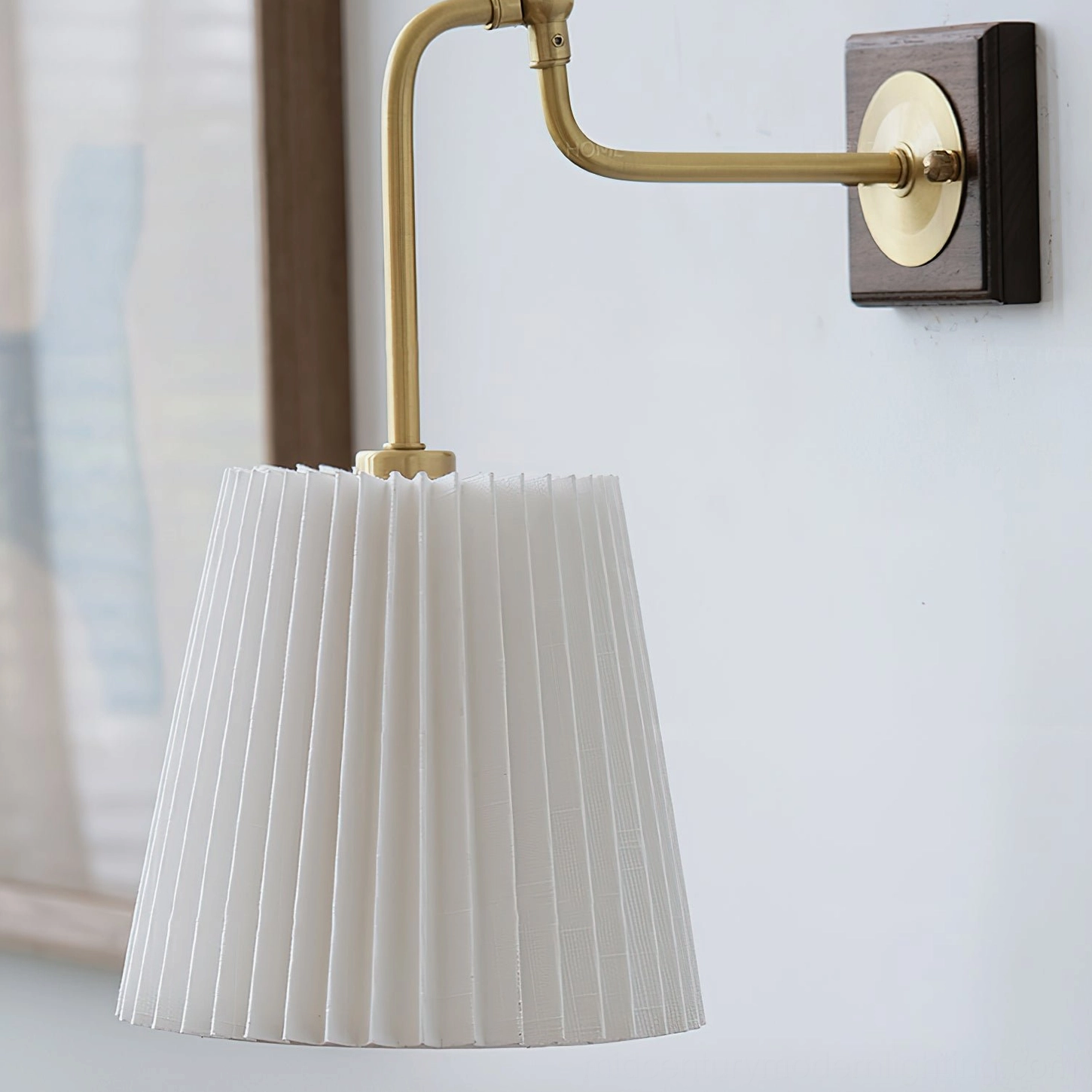 Close-up detail of Argon wall lamp showing accordion pleats of white fabric shade and curved brass arm construction