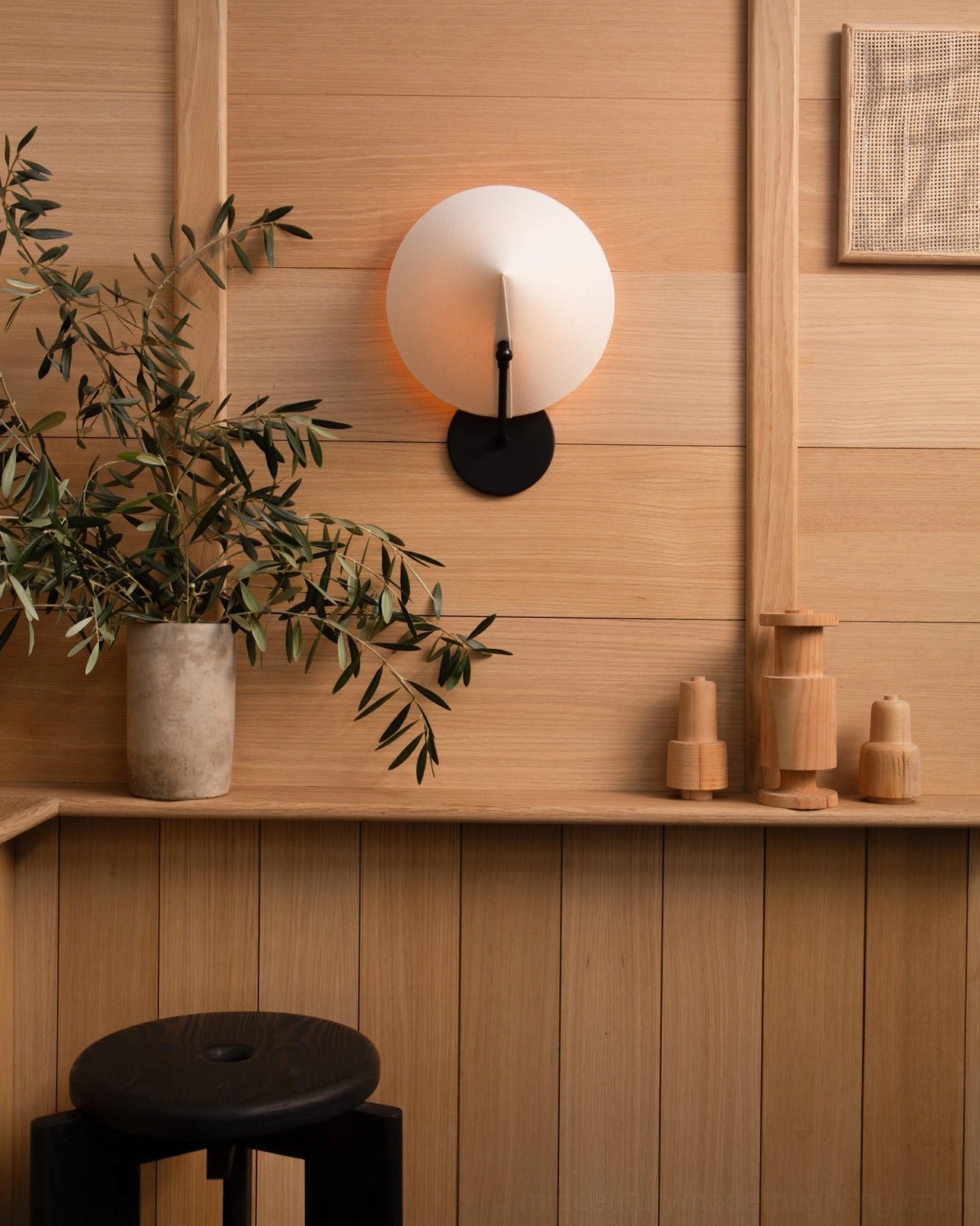 Arno wall sconce with frosted glass globe shade mounted on wooden accent wall in minimalist cafe setting