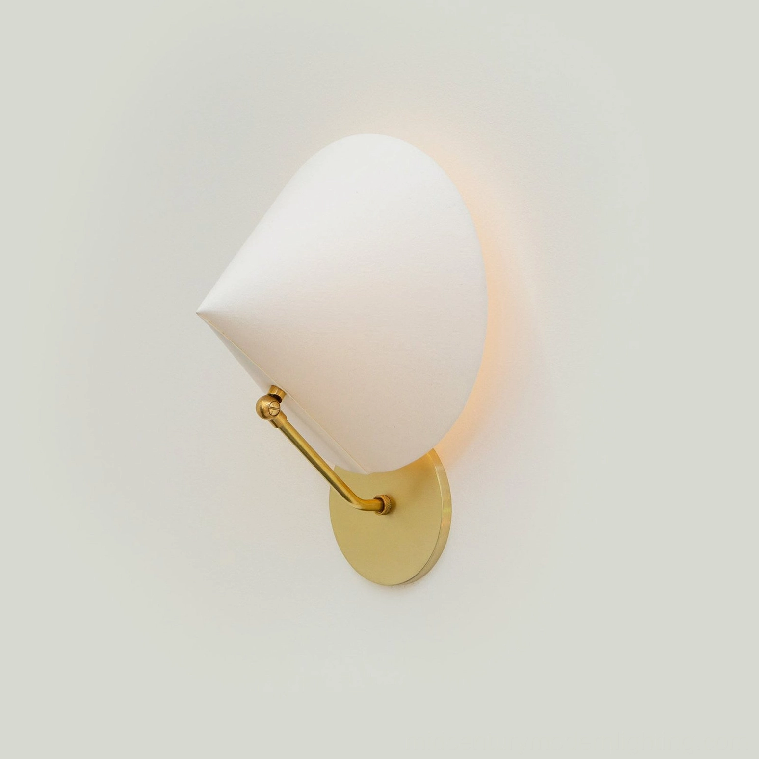 Arno adjustable swivel conical wall sconce with brass finish in warm ambient light, angled detail