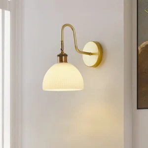 Arren wall-mounted sconce with matte brass finish and off-white ribbed dome shade, side view in bedroom setting