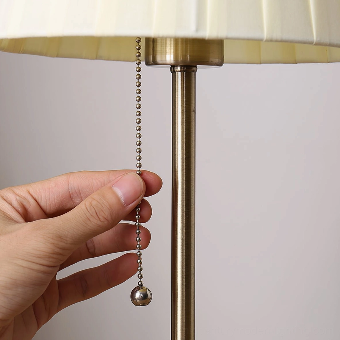 Close-up of Arstid lamp pull chain switch and brass gold metal pole with cream pleated shade