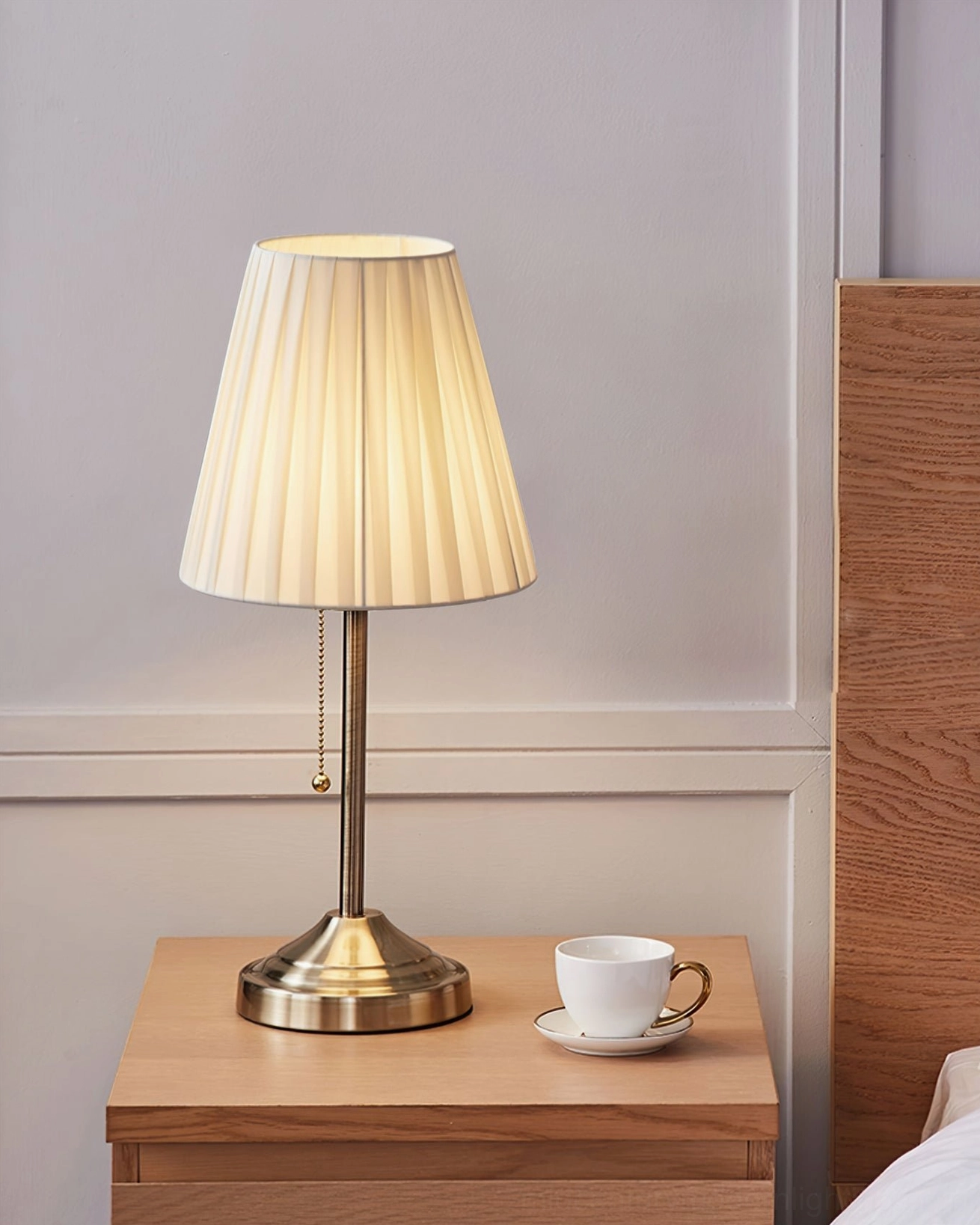 Arstid table lamp side view showing metal base and fabric shade detail with beverage nearby
