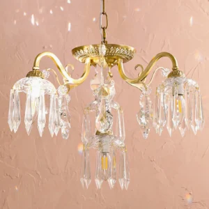 Astrid brass chandelier close-up detail showing warm lit candle bulbs and faceted crystal droplets against pink textured wall
