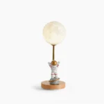 Astronaut moon table lamp with wooden base and LED light, front studio view showing detailed resin astronaut figurine and white lampshade on white background