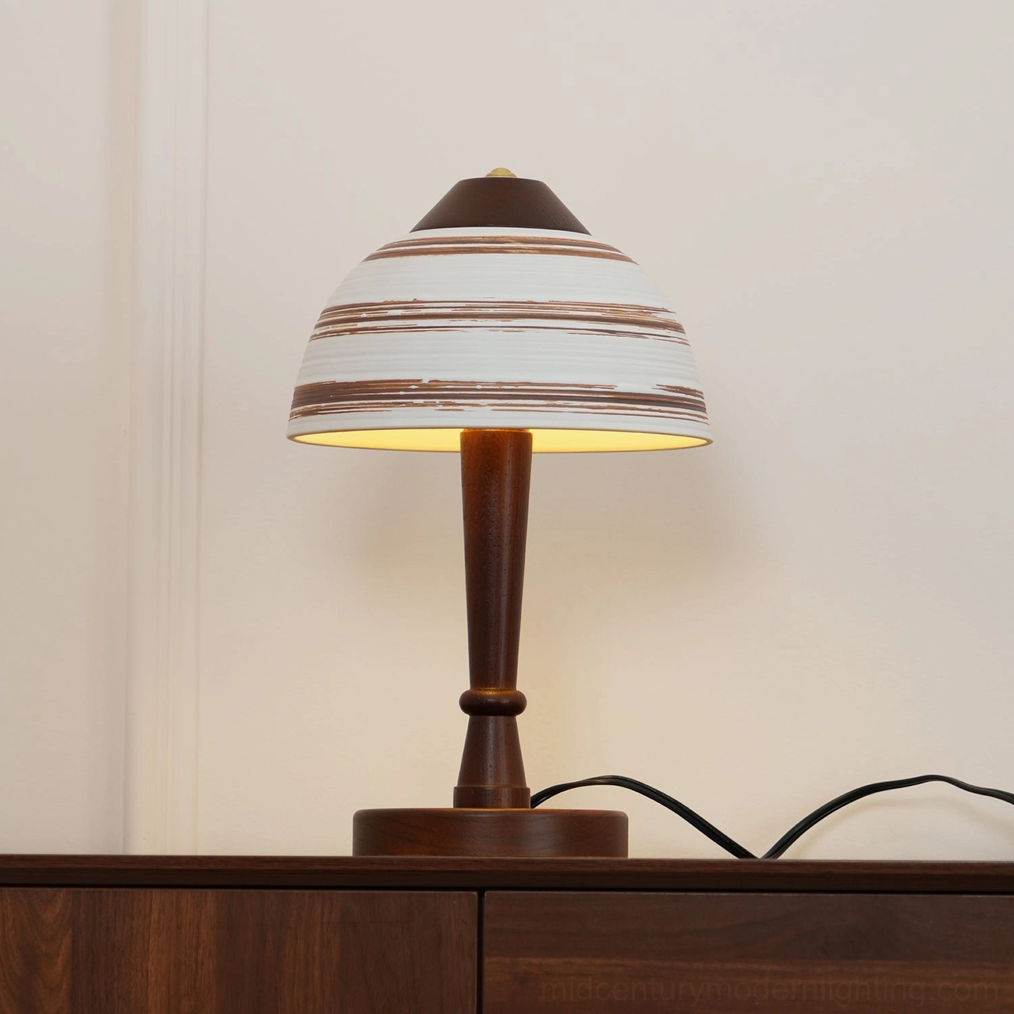Illuminated Athena ceramic table lamp glowing warm light through striped shade on wooden console table