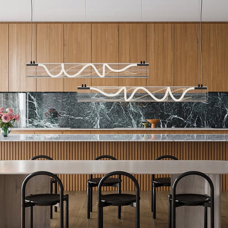 Two Attalea linear chandeliers installed above modern kitchen island with marble backsplash and black bar stools