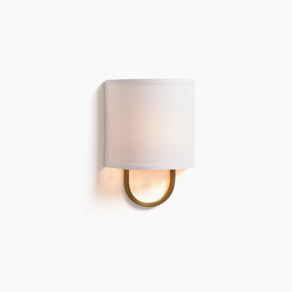Atticus mid-century modern wall sconce with brass U-shaped bracket and off-white fabric drum shade, frontal close-up view