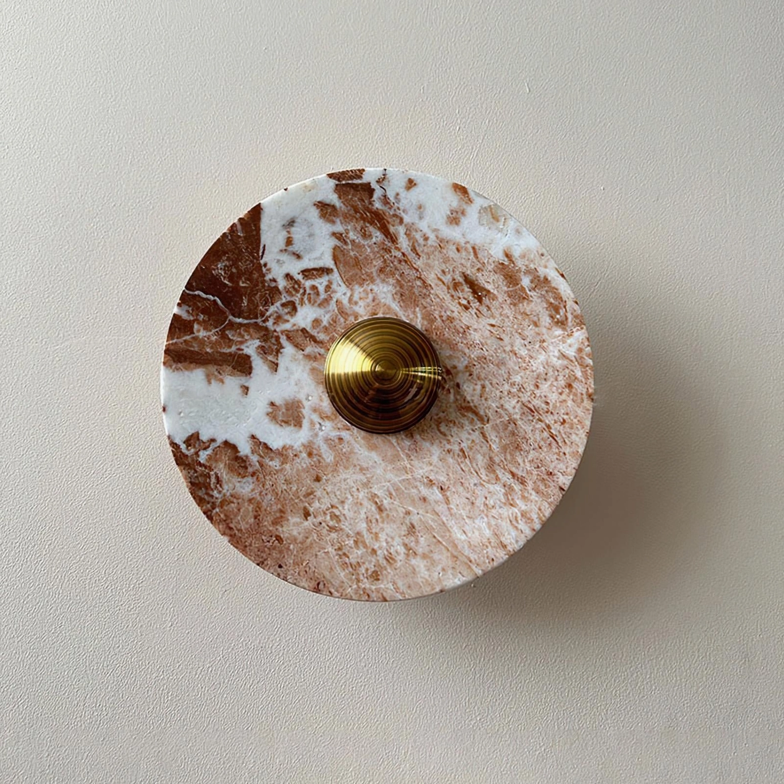 Complete Aurora red marble wall lamp assembly showing full circular form and brass accents on beige wall
