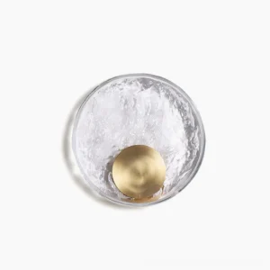 Aurum brass wall sconce with crystalline shade, overhead flat lay view showing circular glass diffuser and brass mounting disk with warm LED backlight