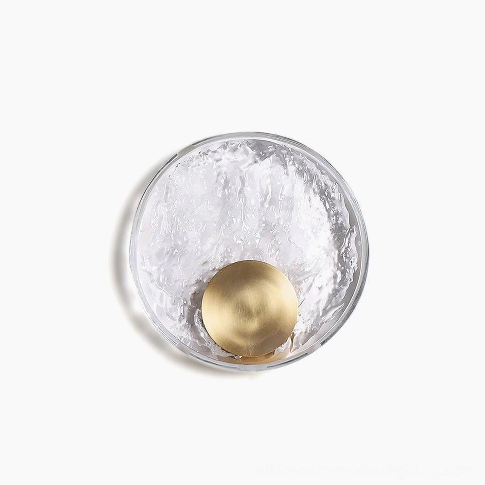 Aurum brass wall sconce with crystalline shade, overhead flat lay view showing circular glass diffuser and brass mounting disk with warm LED backlight