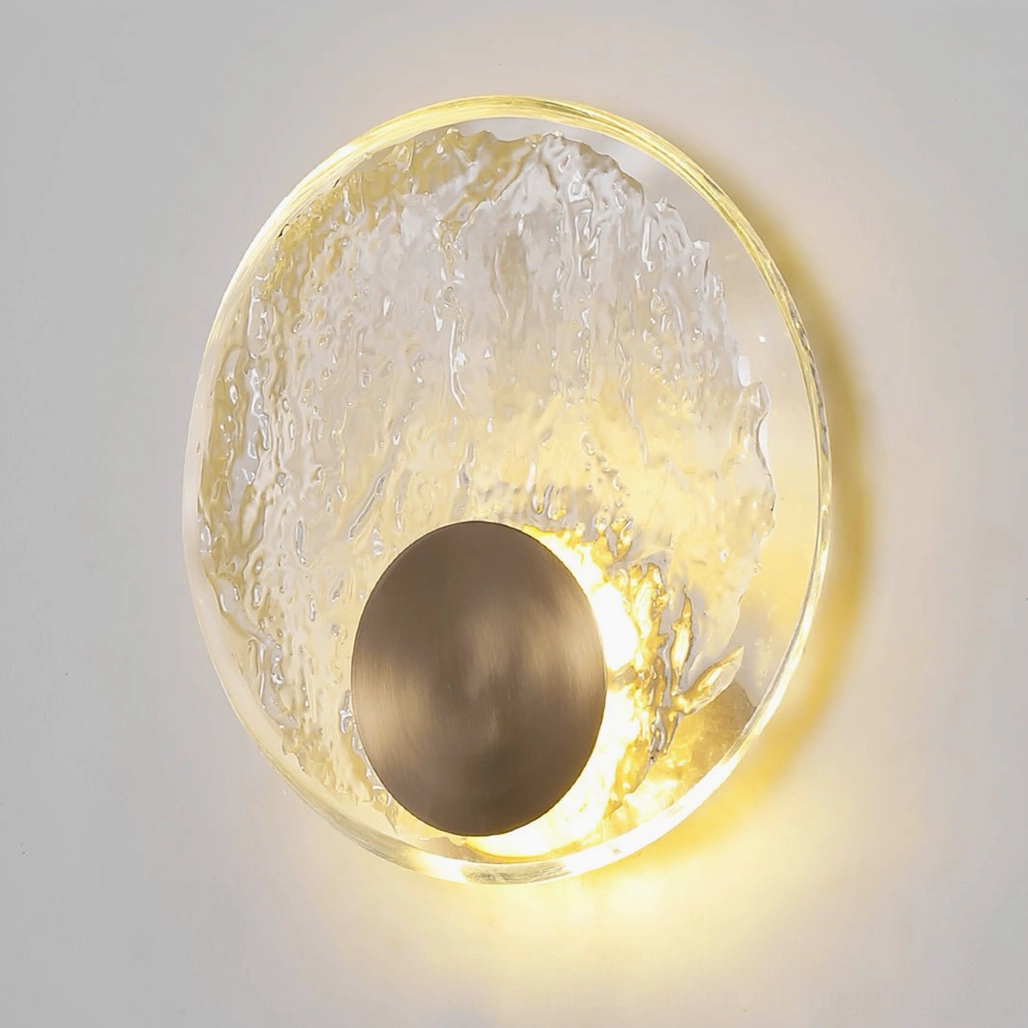Close-up front view of round glass wall sconce with textured crystal shade glowing with warm integrated LED light