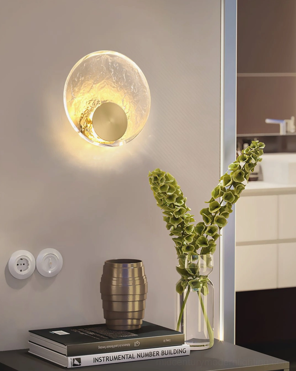 Indoor brass wall light in hallway study corner with tabletop books, metal vase, and green floral arrangement, integrated LED