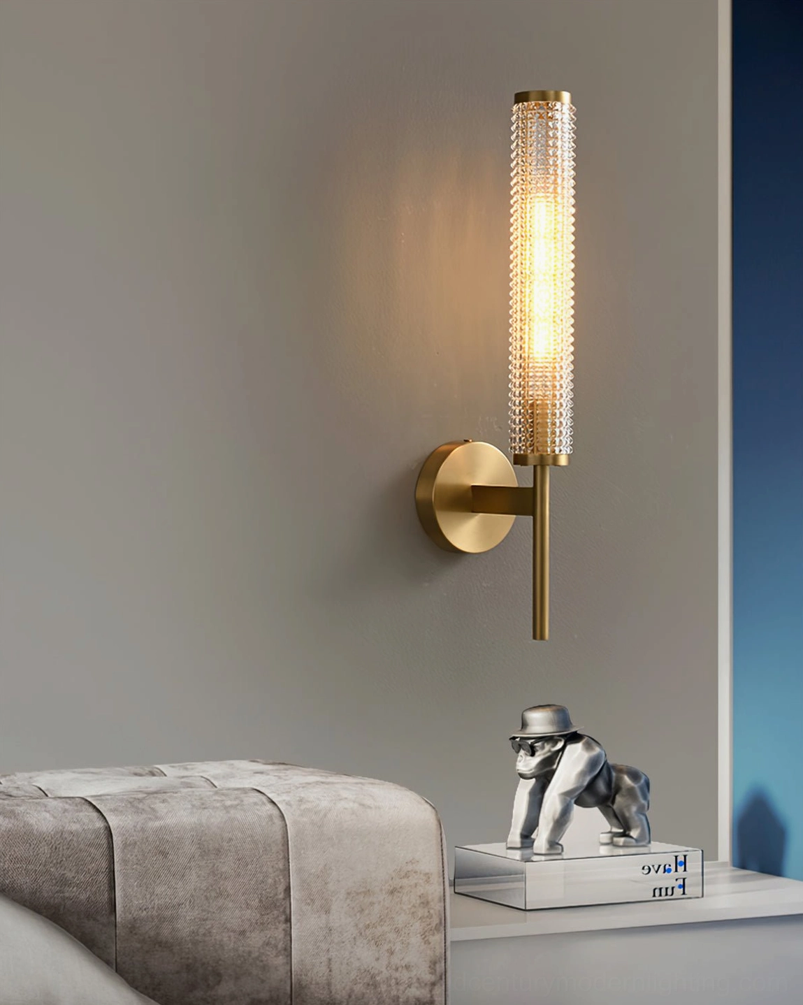 Single Baldassare brass wall lamp glowing above living room shelf corner