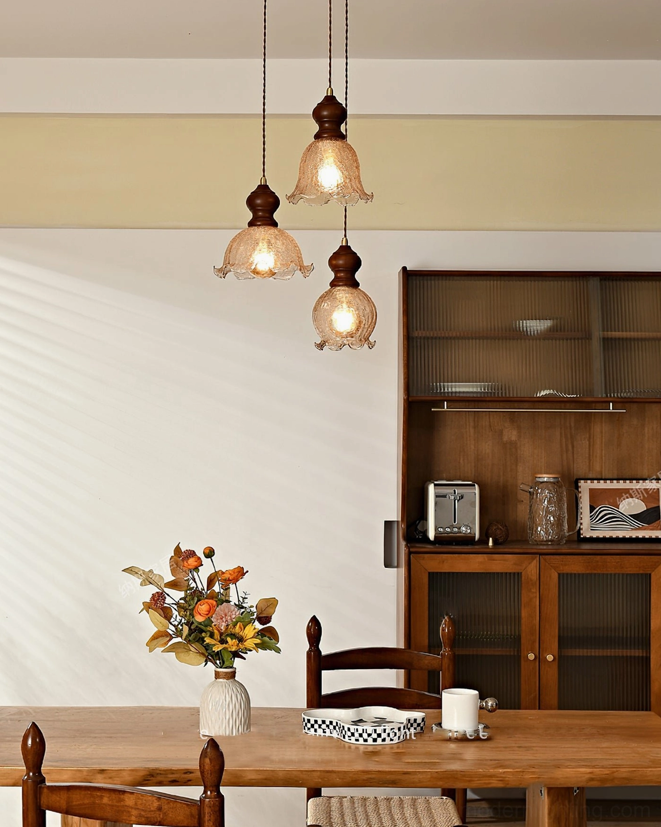 Barron pendant light trio above dining table with wooden storage cabinet and floral arrangements