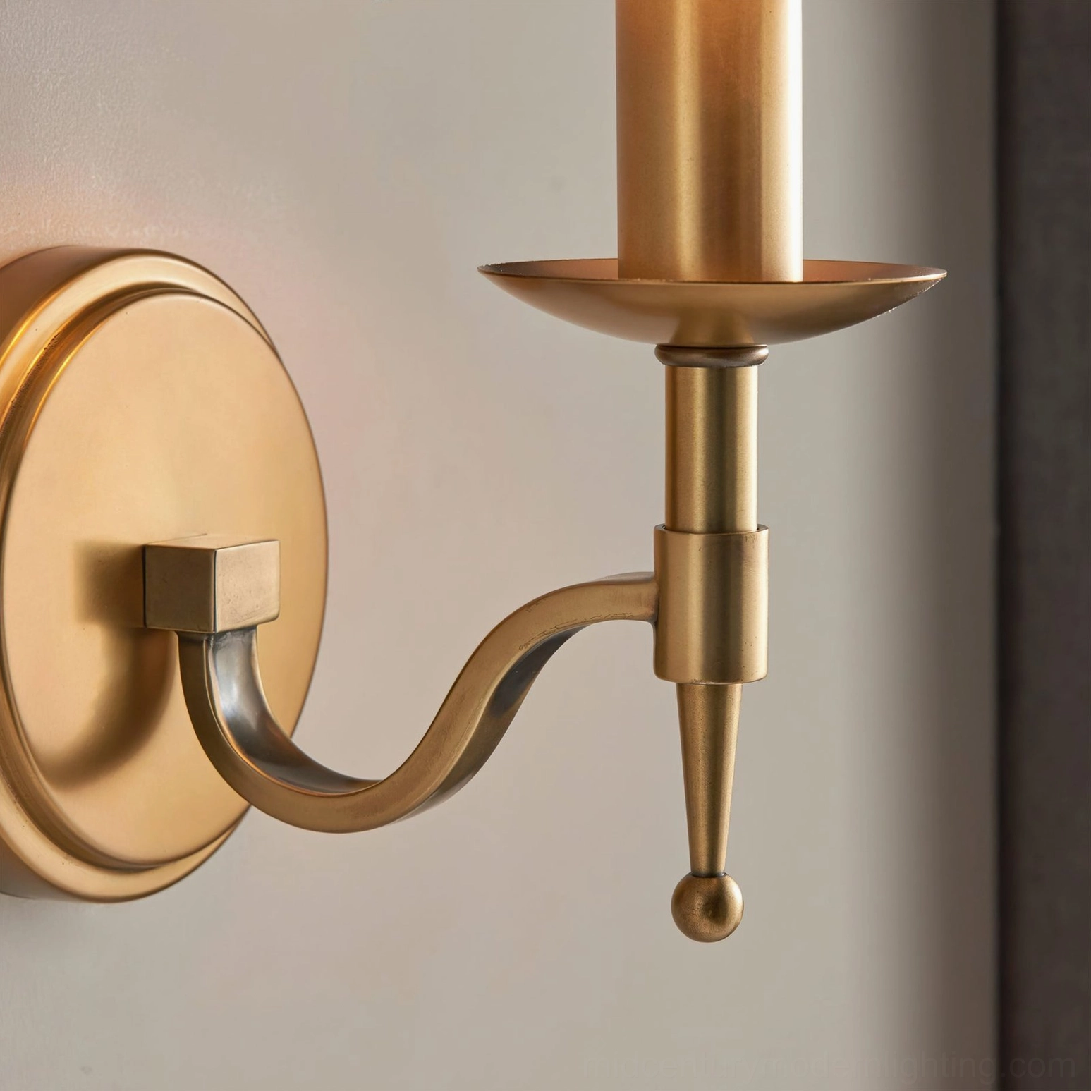 Side angle close-up of Baylor brass wall sconce showing ball finial, curved arm, and round wall plate with dark curtain background