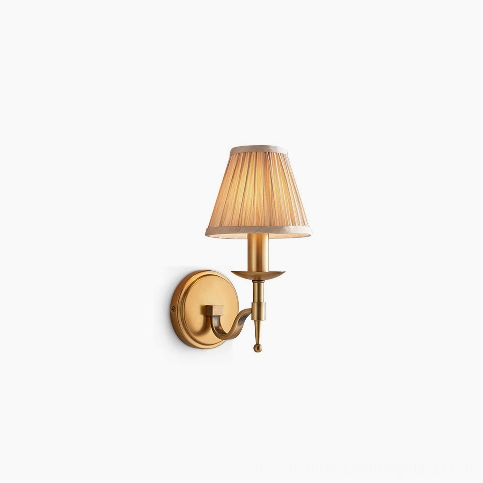 Baylor brass wall sconce with curved arm and pleated beige fabric shade, side front angle view on white background